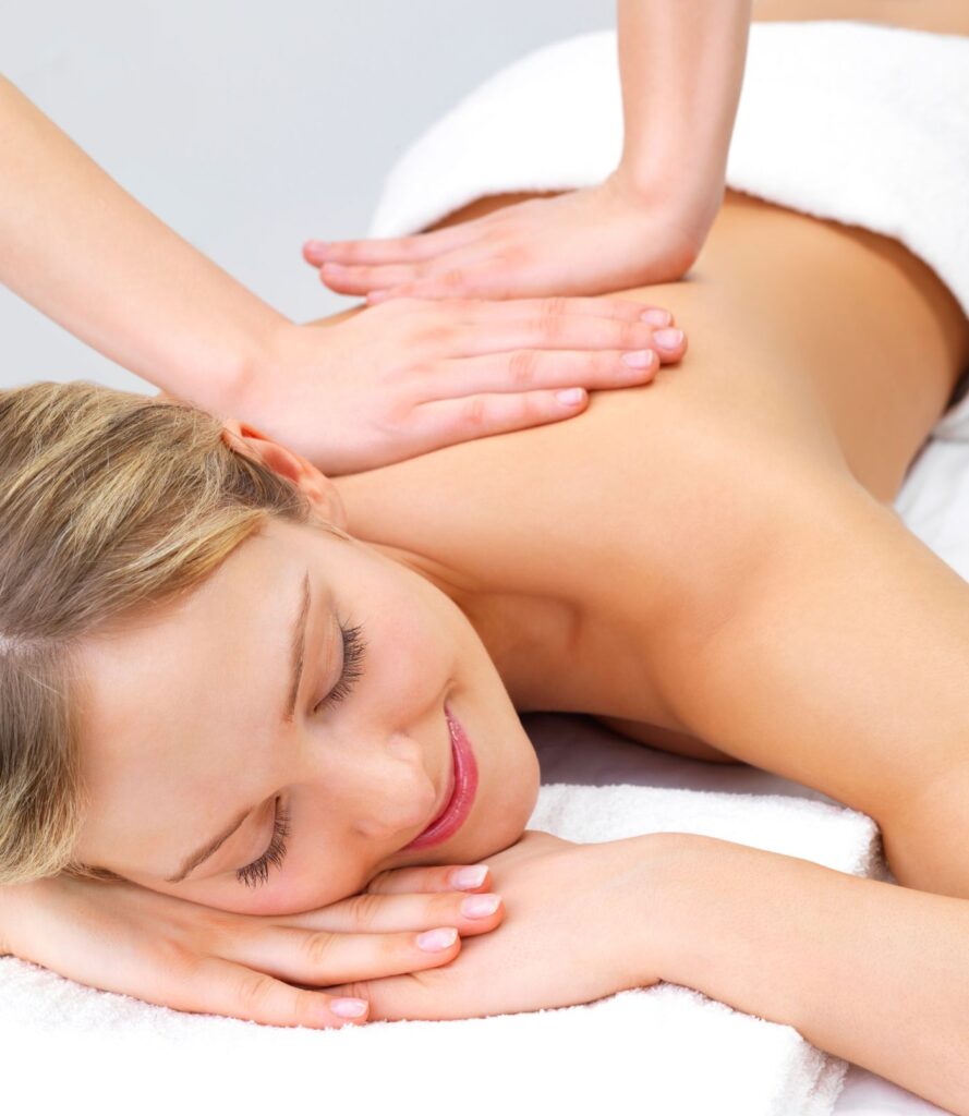 chica rubia sonriente boca abajo sobre una camilla recibiendo un masaje en la espalda